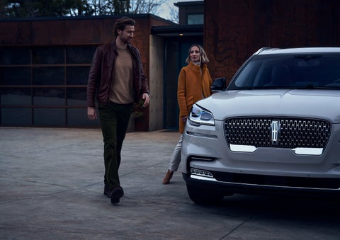 A man and a woman approaching a 2024 Lincoln Aviator® SUV, which illuminates certain lights when they are close | Empire Lincoln of Huntington in Huntington NY